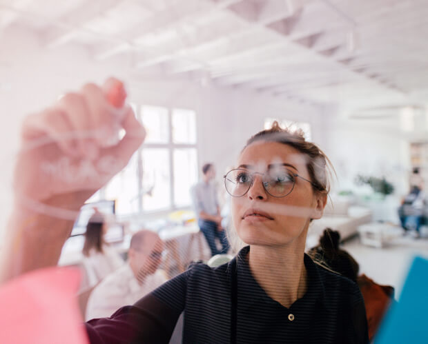 Photo of a lady with glasses writing on a clear board